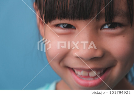 Close-up of smiling young girl revealing her beautiful white teeth on a blue background. Concept of good health in childhood. Close-up of smiling young girl revealing her beautiful white teeth on a blue background. Concept of good health in childhood. 101794923