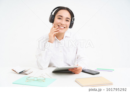People and workplace. Smiling asian woman sits in office, student listening music in headphones and holding digital tablet, white background People and workplace. Smiling asian woman sits in office, student listening music in headphones and holding digital tablet, white background 101795292