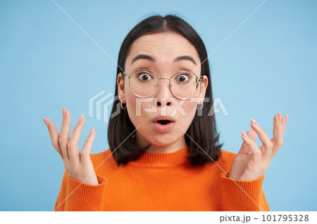 Glasses and eyewear, opticians concept. Portrait of beautiful asian woman in new spectacles, looks surprised, stands over blue background Glasses and eyewear, opticians concept. Portrait of beautiful asian woman in new spectacles, looks surprised, stands over blue background 101795328