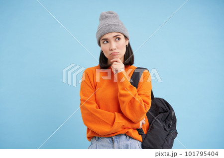Thinking woman in hat, holds backpack, ponders, thinking or making decision, standing over blue studio background Thinking woman in hat, holds backpack, ponders, thinking or making decision, standing over blue studio background 101795404