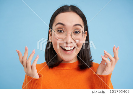 Glasses and eyewear, opticians concept. Portrait of beautiful asian woman in new spectacles, looks surprised, stands over blue background 101795405