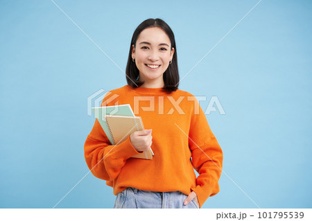 Confident smiling korean woman with notebooks, University student posing against blue background 101795539