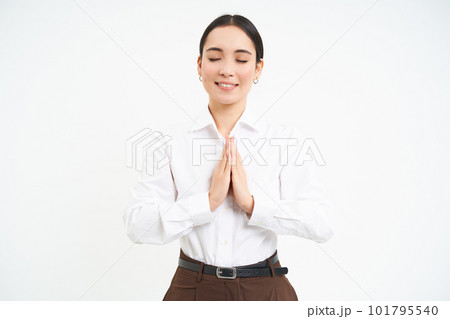 Smiling calm young woman, holds hands in pray with eyes closed, makes wish, hopes for smth, white background 101795540