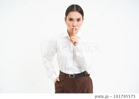 Strict and serious businesswoman shushing, puts finger on lips, tells to be quiet, hush gesture, stands over white background 101795575