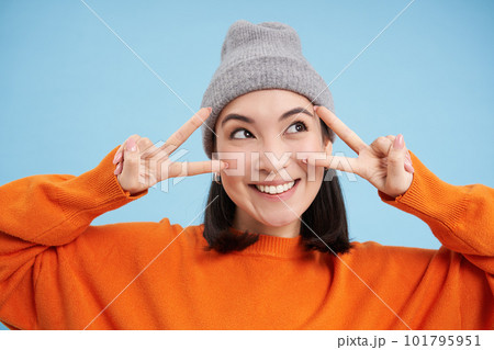 Close up portrait of cute korean girl in beanie, shows peace, vsign gesture, positive vibe, smiling and laughing, posing over blue background Close up portrait of cute korean girl in beanie, shows peace, vsign gesture, positive vibe, smiling and laughing, posing over blue background 101795951