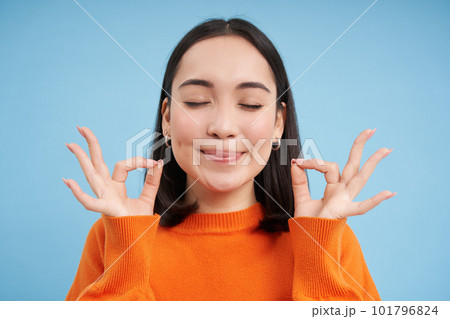 Close up of satisfied smiling asian woman, shows okay, ok sign with pleased face, stands over blue background Close up of satisfied smiling asian woman, shows okay, ok sign with pleased face, stands over blue background 101796824