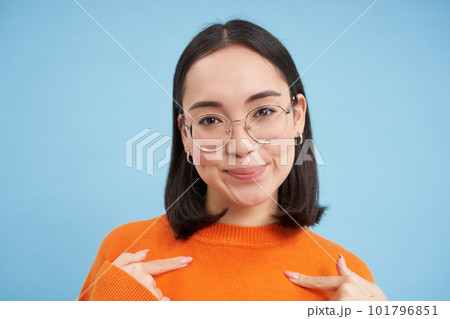 Portrait of beautiful girl in stylish glasses, pointing at herself with confidence, being self-assured, standing over blue background 101796851