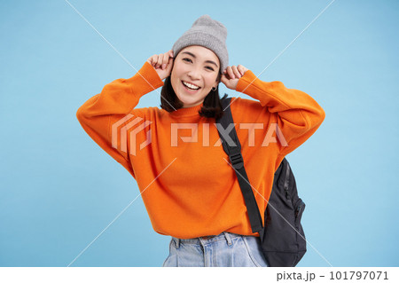 Stylish young asian woman in warm hat, walking with backpack, going somewhere with bag, standing over blue studio background Stylish young asian woman in warm hat, walking with backpack, going somewhere with bag, standing over blue studio background 101797071