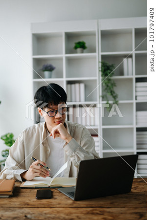 Male student taking notes from a book at library, Young asian sitting at desk doing assignments in college library 101797409