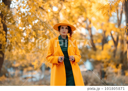 Beautiful woman walks outdoors in autumn. She is wearing a yellow coat, yellow hat and green dress. Young woman enjoying the autumn weather. Autumn content 101805871