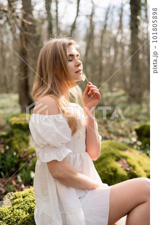 Snowdrops galanthus blonde. A girl in a white dress sits on a meadow with snowdrops in a spring forest 101805898
