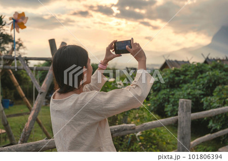 Young asian woman in casual cloth taking a photo with smartphone on hill in tropical rainforest 101806394