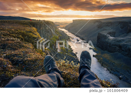 Legs of hiker man sitting on edge of mountain with waterfall flowing in canyon on Icelandic Highlands in the evening at Sigoldugljufur 101806409