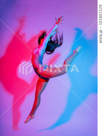 A girl gymnast in a swimsuit does tricks on a white and dark background. Front view A girl gymnast in a swimsuit does tricks on a white and dark background. Front view 101807229