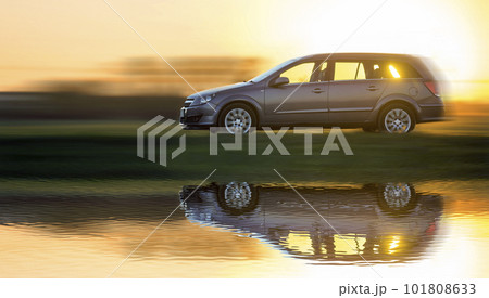 Long exposure shot of gray silver car moving fast in countryside on blurred bright orange clear sky at sunset copy space background. Transportation, speed, traveling, vehicles design concept. Long exposure shot of gray silver car moving fast in countryside on blurred bright orange clear sky at sunset copy space background. Transportation, speed, traveling, vehicles design concept. 101808633