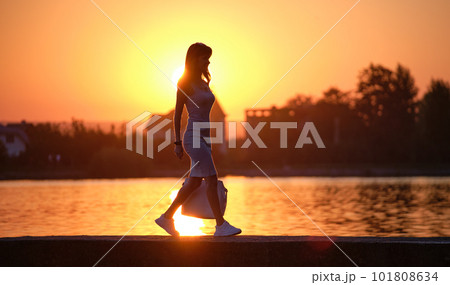 Lonely young woman walking alone on lake shore enjoying warm evening. Wellbeing and relaxing in nature concept. 101808634
