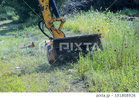 An employee of utility company mowing tall grass along side road using professional tractor mechanical mower cut grass 101808926
