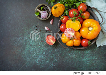Various colorful tomatoes and parsley leaves on a dark stone background. Organic food. View from above. Copy space. Various colorful tomatoes and parsley leaves on a dark stone background. Organic food. View from above. Copy space. 101809738