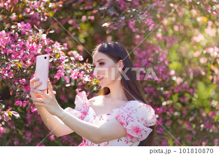 girl is standing near a pink blooming apple tree with smartphone 101810870