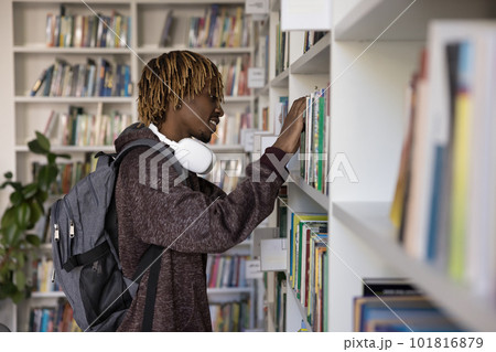 African hipster student guy chooses textbook standing alone in library African hipster student guy chooses textbook standing alone in library 101816879