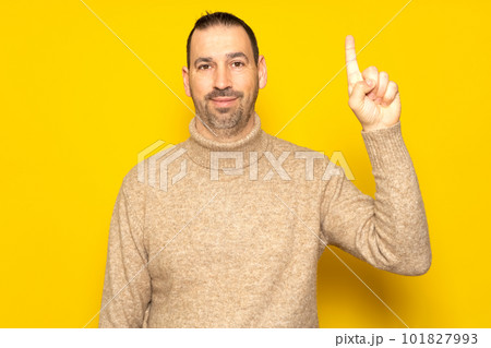 Insightful smart proactive caucasian man 40s wearing a turtleneck holding index finger up with a great new idea isolated on yellow background studio portrait. People lifestyle concept. Insightful smart proactive caucasian man 40s wearing a turtleneck holding index finger up with a great new idea isolated on yellow background studio portrait. People lifestyle concept. 101827993