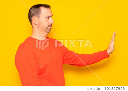 Hispanic man with a beard in his 40s wearing a red sweater gesturing stop while standing in profile, isolated over yellow background. Hispanic man with a beard in his 40s wearing a red sweater gesturing stop while standing in profile, isolated over yellow background. 101827996