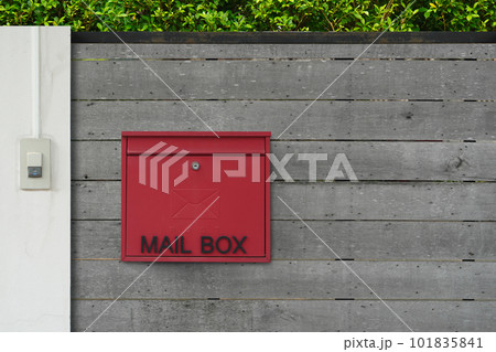 red and black mailbox hangs on the wooden fence door in front of the house, wall green tree background, object, decor, modern, copy space 101835841