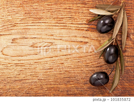 Olives over Wooden Background. Dark olives with leaves on wooden background, old wooden table, olive branch, background. top view, flat lay 101835872