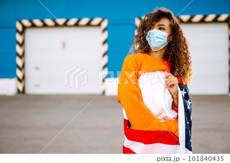 African American woman with medical face mask posing with american flag.The concept of preventing the spread of the epidemic. Covid-2019. African American woman with medical face mask posing with american flag.The concept of preventing the spread of the epidemic. Covid-2019. 101840435
