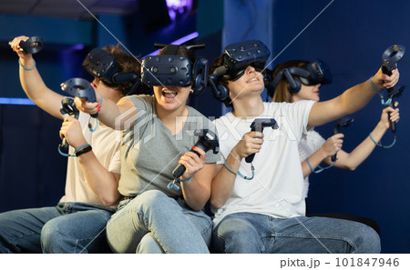 group of four friends wearing virtual reality glasses and with joysticks sit and play dynamic game group of four friends wearing virtual reality glasses and with joysticks sit and play dynamic game 101847946