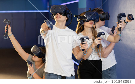 group of four friends wearing virtual reality glasses and with joysticks are playing dynamic game group of four friends wearing virtual reality glasses and with joysticks are playing dynamic game 101848092