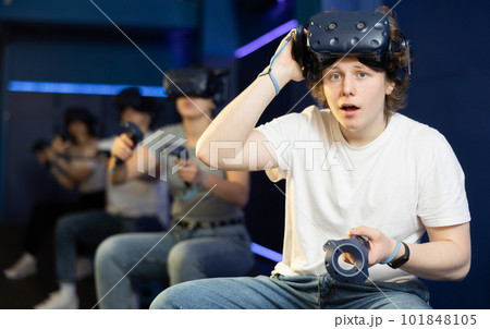 Emotional young guy in VR headset with joysticks playing with friends Emotional young guy in VR headset with joysticks playing with friends 101848105