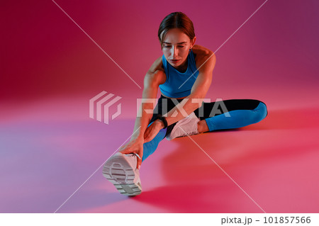 Healthy fitness woman wearing sportswear sitting on floor and stretching leg on studio background Healthy fitness woman wearing sportswear sitting on floor and stretching leg on studio background 101857566