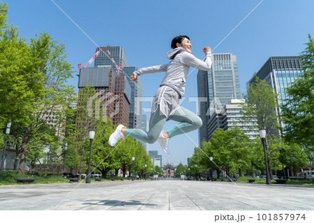 オフィス街の公園でジャンプするミドルエイジの女性 オフィス街の公園でジャンプするミドルエイジの女性 101857974
