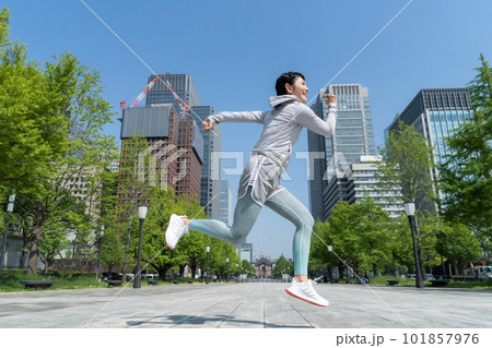 オフィス街の公園でジャンプするミドルエイジの女性 オフィス街の公園でジャンプするミドルエイジの女性 101857976