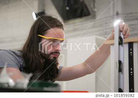 Professional carpenters using a ruler and spirit level to measures a wood panel. Professional carpenter measuring a wood plank. Professional carpenters using a ruler and spirit level to measures a wood panel. Professional carpenter measuring a wood plank. 101859382