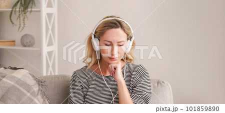 Music healing. Upset woman. Sound recovery. Depressed lady listening favorite melody on headphones sitting in light room interior. 101859890