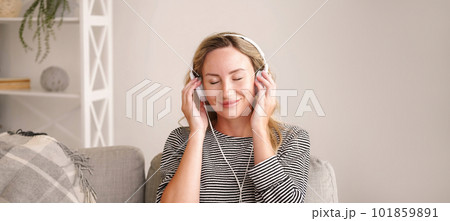 Pleasant music. Inspired woman. Stereo sound. Happy relaxed lady listening favorite song on headphones closing eyes in light room interior. 101859891