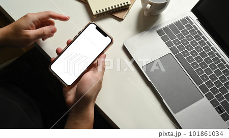 Man holding smartphone with empty screen on workspace with top view. 101861034