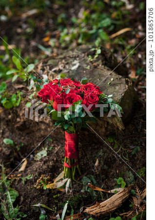 Two golden wedding rings on a stump, in the background a bouquet with red roses 101865706