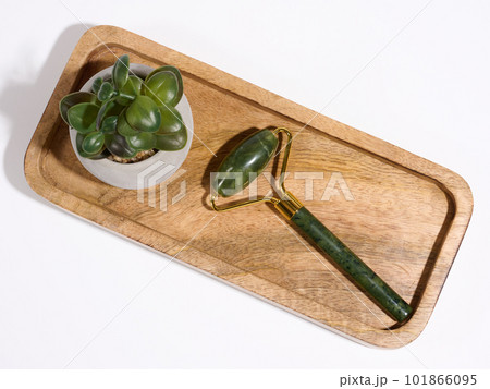 Jade facial massager, an item for cosmetic procedures on a brown wooden plate, top view Jade facial massager, an item for cosmetic procedures on a brown wooden plate, top view 101866095