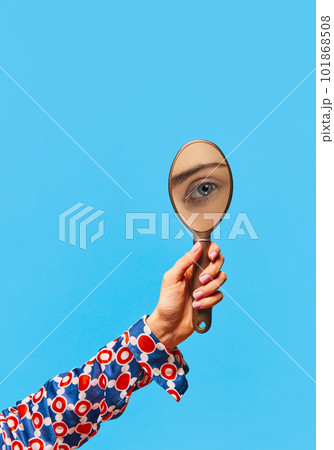 Female hand holding small mirror with reflection of gorgeous woman's eye over bright blue background. Eyebrow lamination Female hand holding small mirror with reflection of gorgeous woman's eye over bright blue background. Eyebrow lamination 101868508