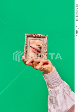 Female hand holding small mirror with reflection of beautiful woman's lips with natural make up over green background. Lip volumizing 101868518