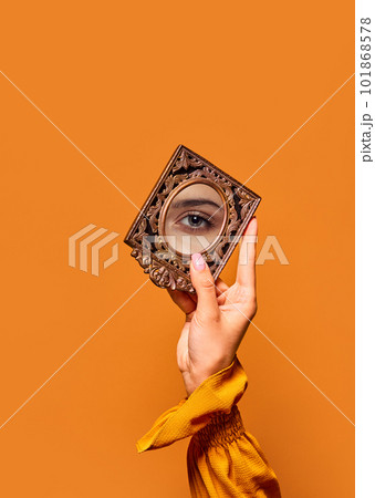 Female hand holding small mirror with reflection of beautiful, green girl's eye over orange background. Eyelash lamination Female hand holding small mirror with reflection of beautiful, green girl's eye over orange background. Eyelash lamination 101868578