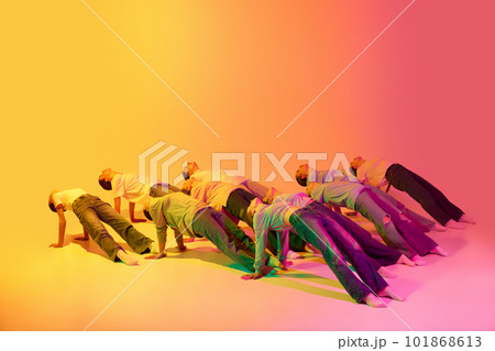 Portrait with group of teenagers, young dancers laying on floor in figures together over pink and yellow gradient background in neon light. Modern dance style 101868613