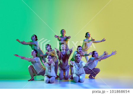 Group of young adorable girls moving to the beat of the music on gradient background in neon light. Teenage choreography studio 101868654