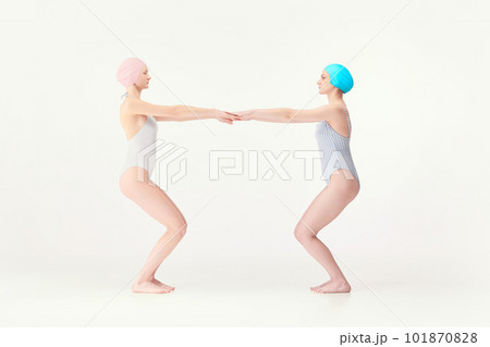 Two young girls, swimming athletes in retro style swimsuits standing in jump position isolated over white background 101870828