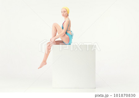 Young tender girl sitting in blue retro style swimsuit and yellow swimming cap isolated over white background. Summer vacation. 101870830