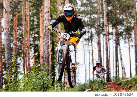 male racer athlete riding downhill race, jump over hill, on him protection jacket, and knee, shin guard 101872624