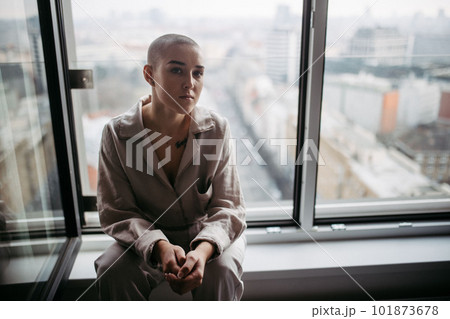 Young unhappy woman with cancer sitting in a window and looking at view. 101873678